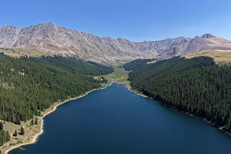 Clinton Gulch Reservoir seen from the air, deep blue water in a forested valley below a high rocky crest