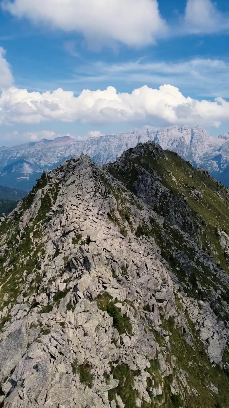 A knife-edge rock ridge with a small iron summit marker, the Brenta Dolomites pale on the far skyline