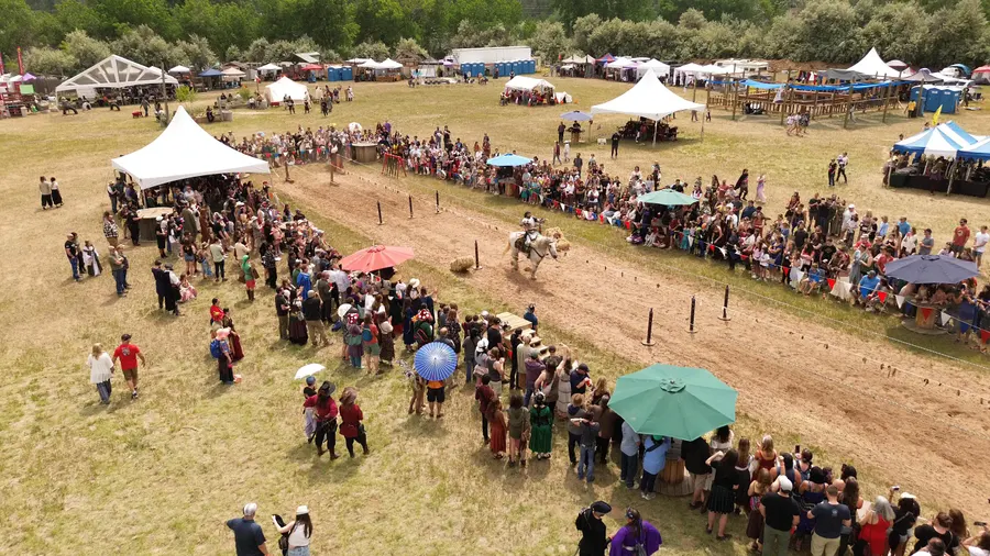 Aerial view of a knight on a white horse charging down the jousting lane between festival crowds