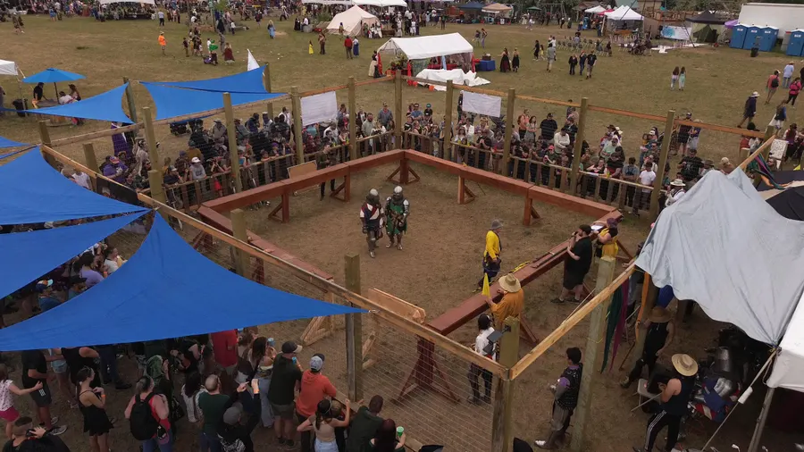 Aerial view of two armored fighters squaring up in the wooden combat arena, a marshal in yellow between them