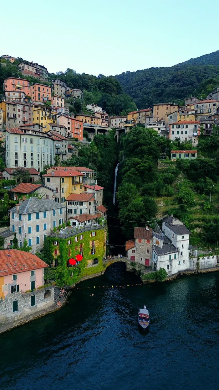 The village of Nesso on Lake Como, the Civera bridge over the gorge waterfall and a boat on the water below