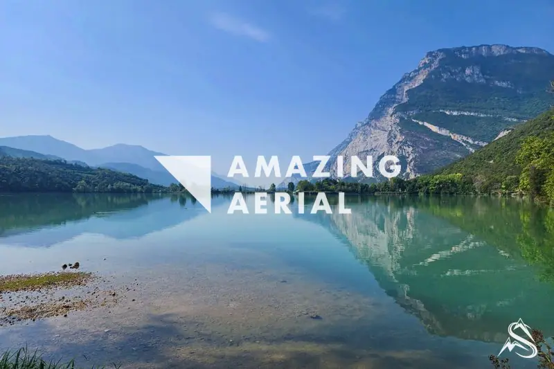 Lake Toblino under a steep wooded mountain, the peak mirrored in the still green water