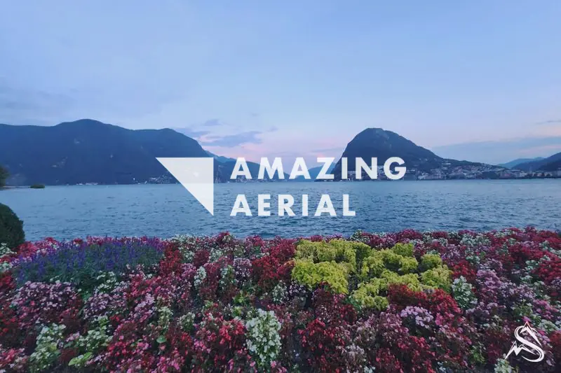 Red flowerbeds along the Lugano lakefront at dusk, the lake and its mountains beyond