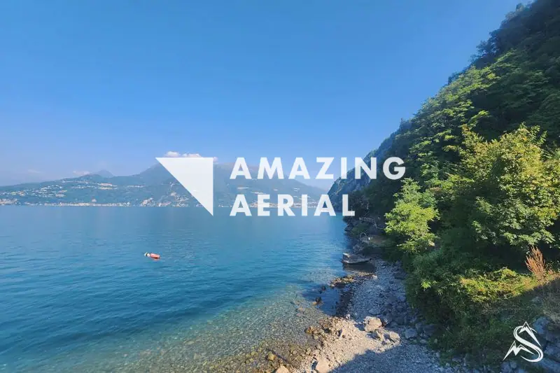 A rocky, wooded shore of Lake Como near Varenna, clear water and distant mountains