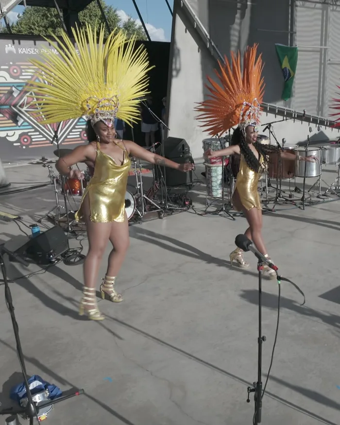 Two dancers in gold dresses and yellow and orange feathered headdresses dancing together on stage