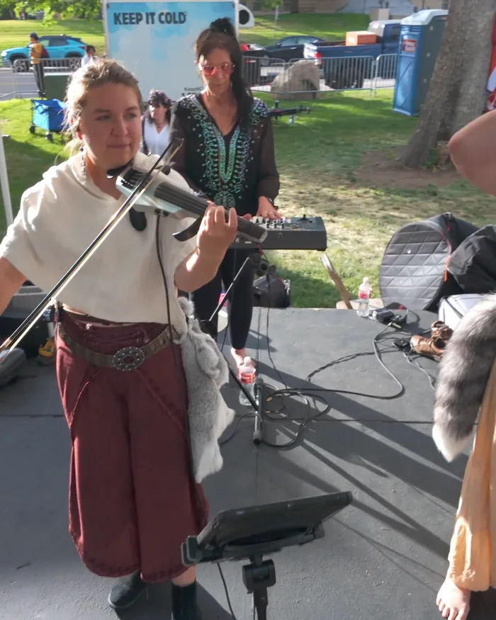 Nordic Daughter's violinist and keyboardist performing on the festival stage, the festival grounds and Nordic flags visible behind them