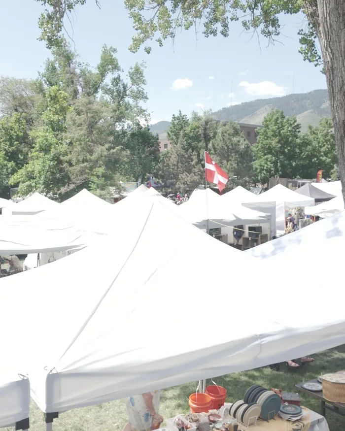 A wide view over the festival's white vendor tents, a Danish flag flying above the market and the Golden foothills behind