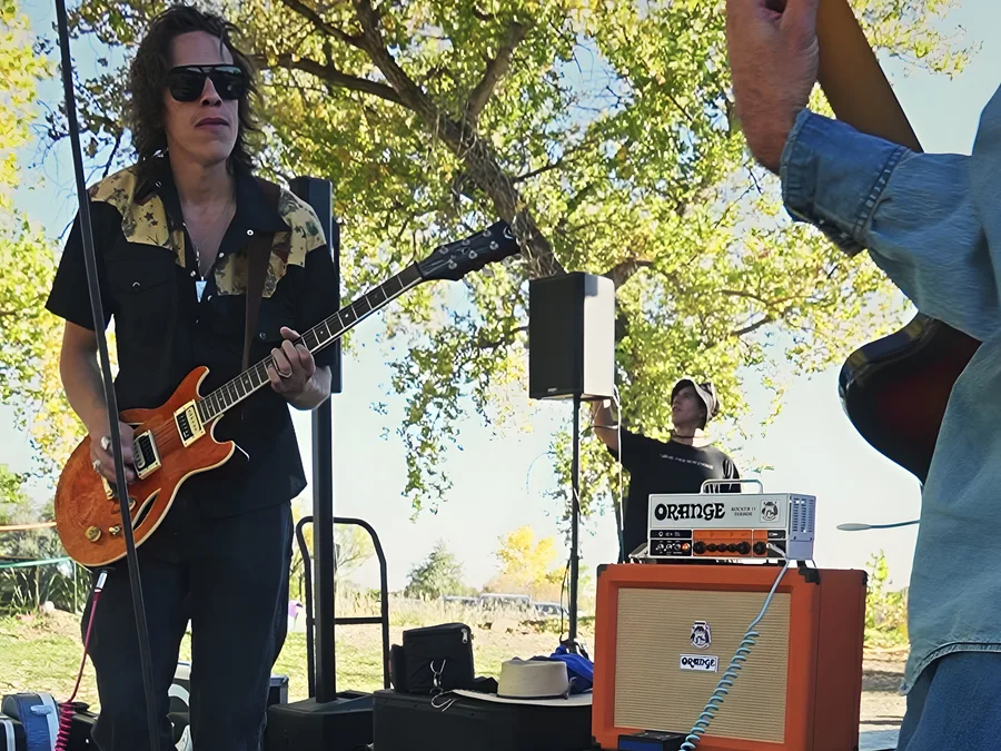 A guitarist playing in a live band at golden hour at the 2023 Vybe festival, sunlight through the fall trees