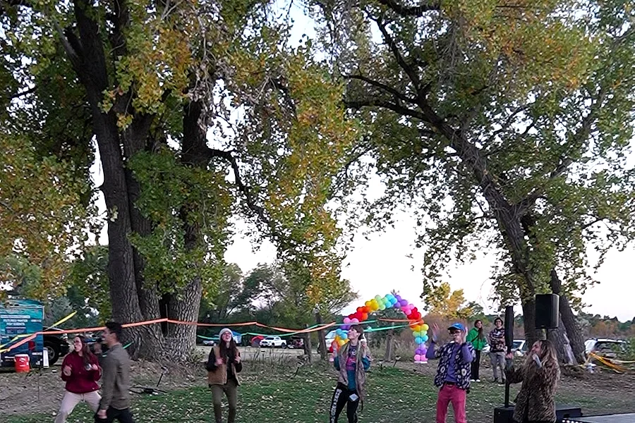 A group practicing flow arts at dusk under the trees, a rainbow balloon arch behind them