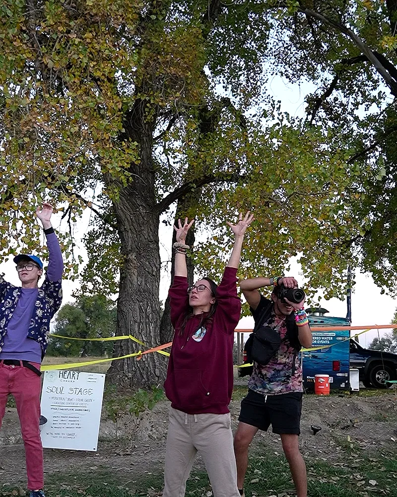 Three festivalgoers with arms raised together in front of a hand-lettered Soul Stage sign under the fall trees