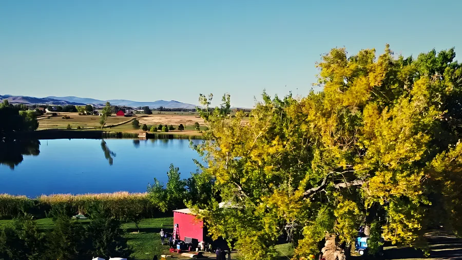An aerial view of the Vybe festival grounds beside a lake in fall, a stage tent and parked cars below distant foothills
