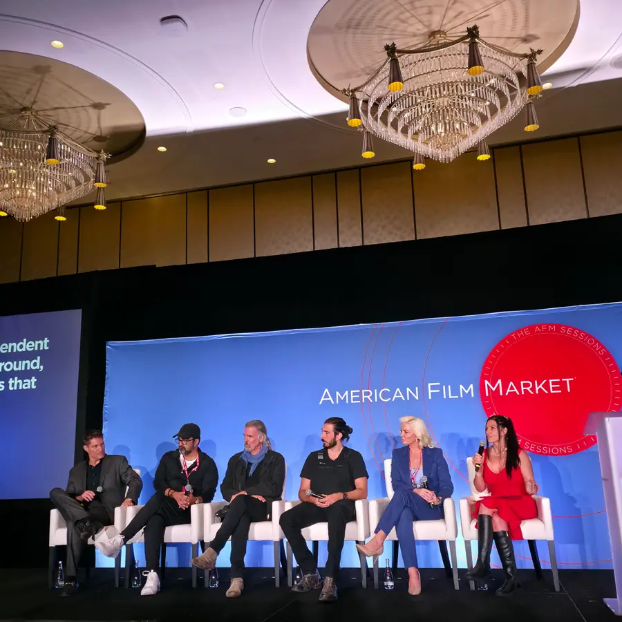 The same six panelists from closer in, a caption slide visible on the side screen.