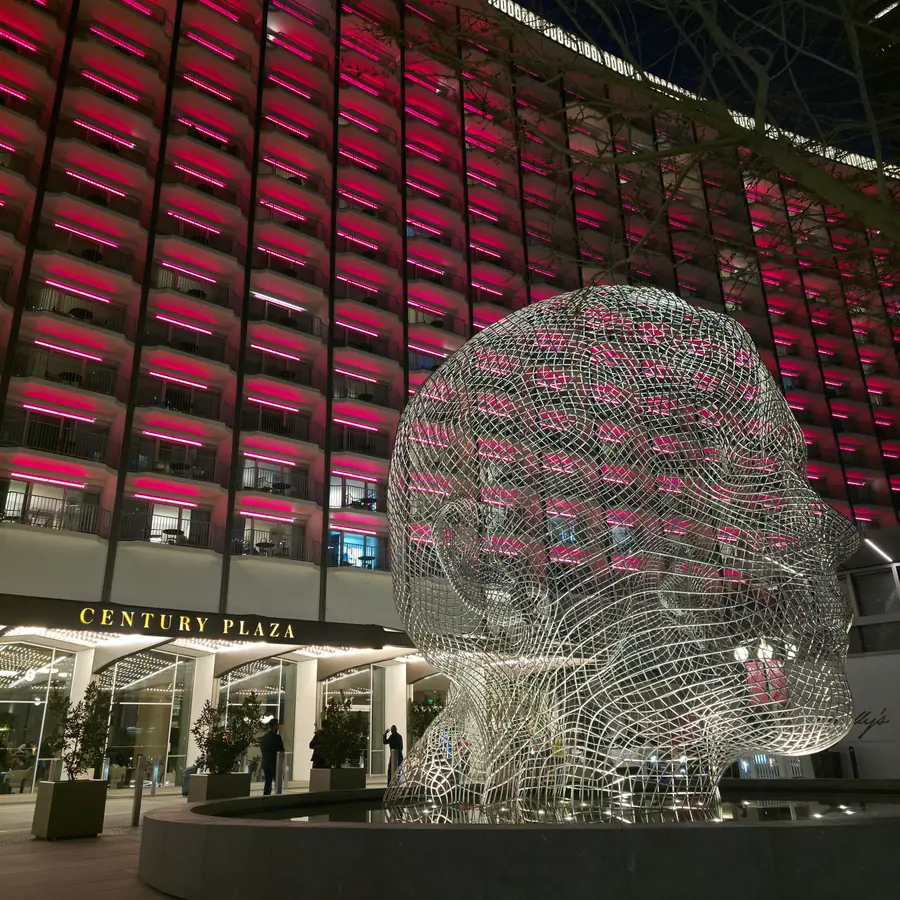The Fairmont Century Plaza hotel exterior at night, lit facade and a large woven-wire sculpture out front.