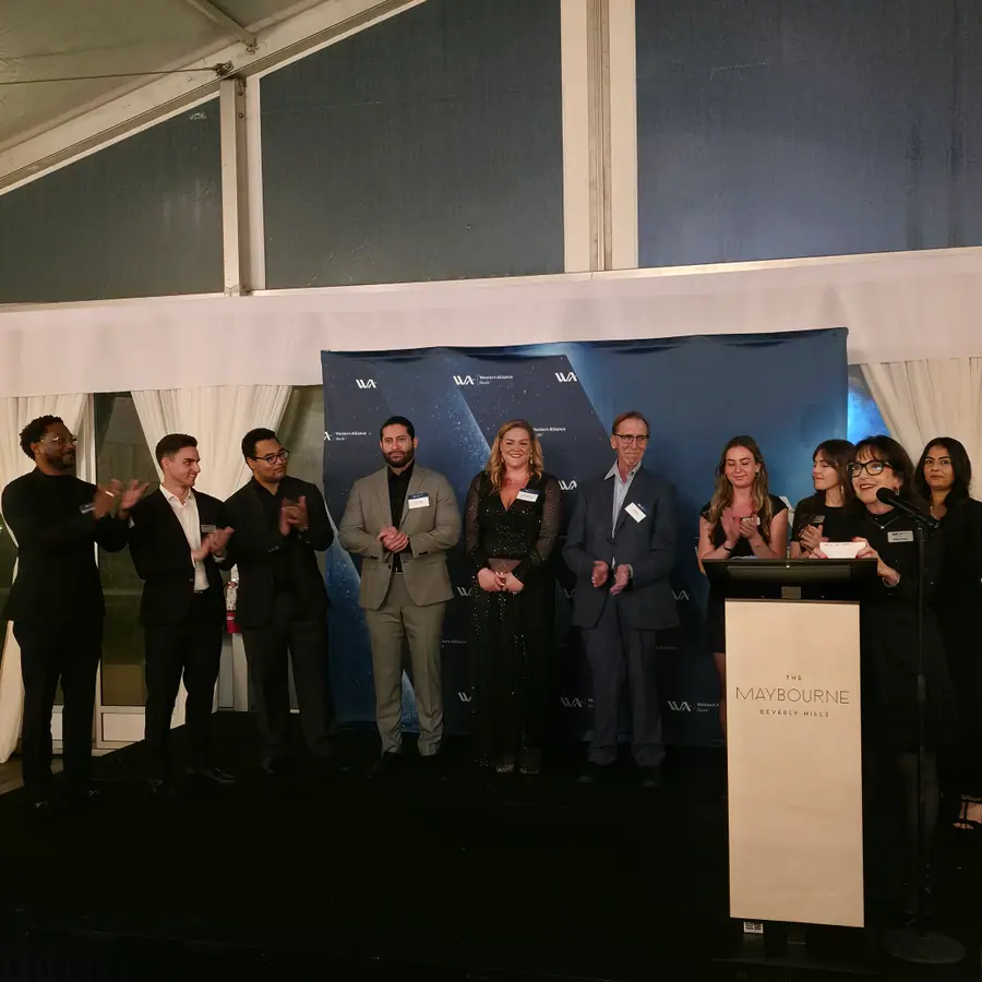A line of hosts and guests on a small stage under a Western Alliance Bank backdrop, one speaking from a Maybourne Beverly Hills lectern.