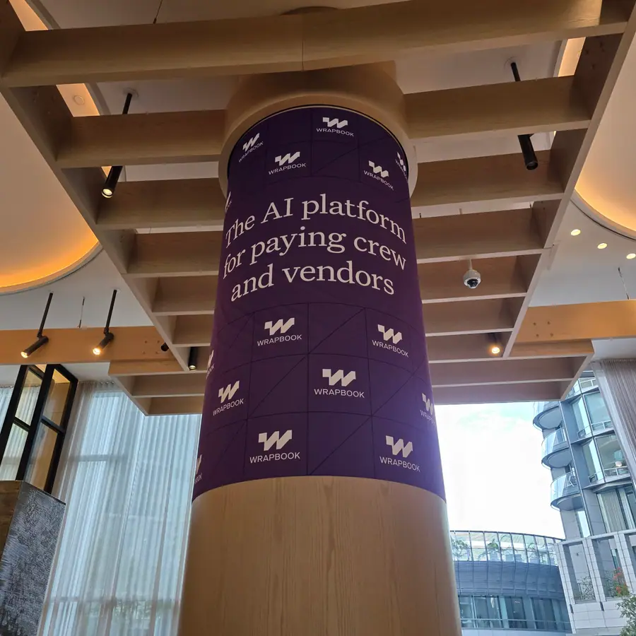 A hotel lobby column wrapped in Wrapbook branding reading “the AI platform for paying crew and vendors.”