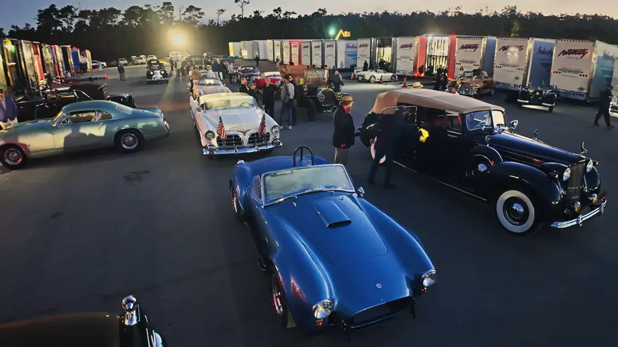 A dark blue Cobra roadster queued in a line of pre-war cars at dusk-blue light, transporters queued behind