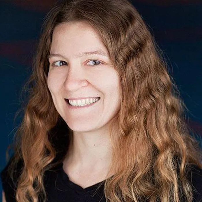 Portrait of Amber MacPherson, long wavy brown hair, smiling, black top, dark blue background.