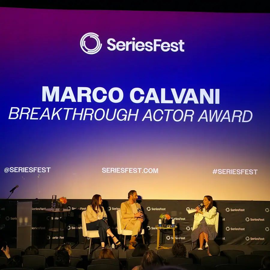 The SeriesFest screen reading “Marco Calvani — Breakthrough Actor Award,” a panel seated below it.