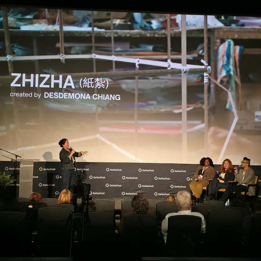 A creator speaking from the stage in front of a still from Zhizha, the screen crediting Desdemona Chiang.