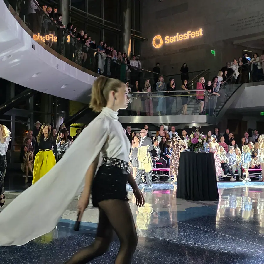 A model mid-stride on the runway, a long white cape trailing behind her.