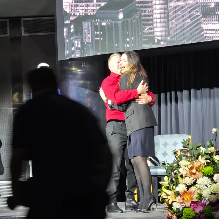 Two people embracing on stage after the honoring, the audience watching from below.