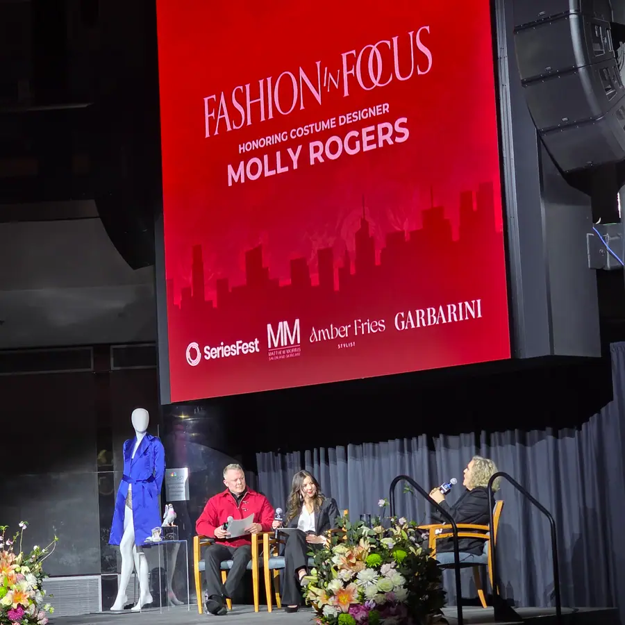 The Fashion in Focus titlecard reading Honoring Costume Designer Molly Rogers, three panelists seated below beside a mannequin in a blue coat.