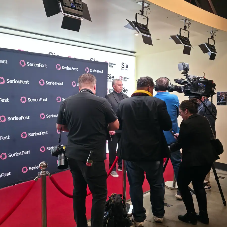 A press scrum working the step-and-repeat, cameras and boom mics raised.
