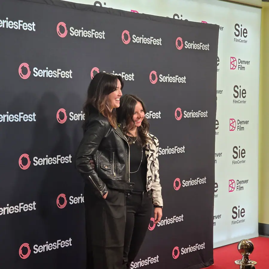 Two guests posed at the SeriesFest premiere wall, Denver Film and Sie FilmCenter branding beside them.