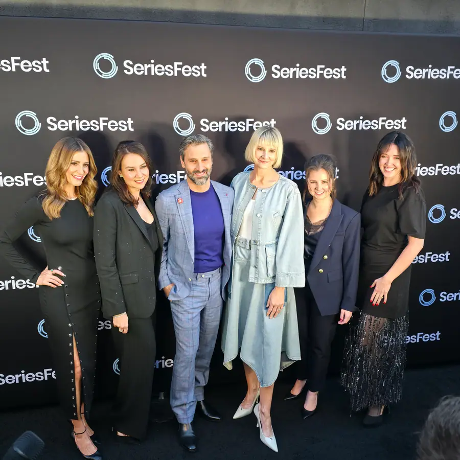 Six members of a cast and producing team lined up on the SeriesFest red carpet at Season 12's opening night, the SeriesFest step-and-repeat behind them.