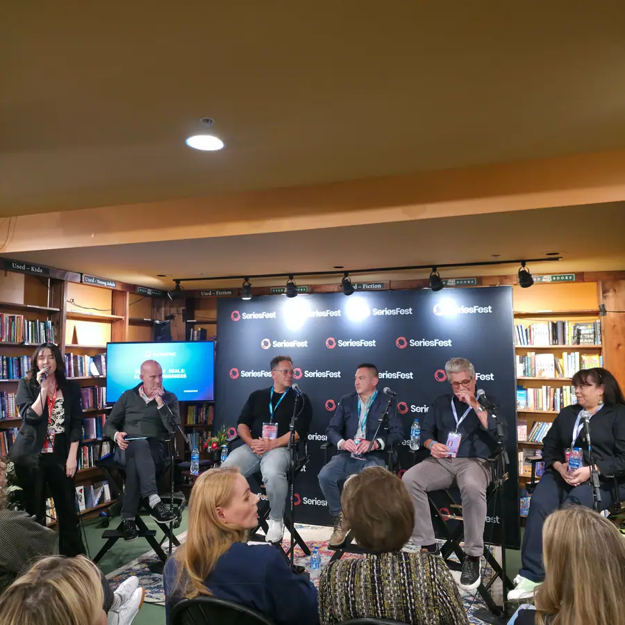 A panel of six on stage at a bookstore venue, the screen behind reading Behind the Deals: Agents & Managers.