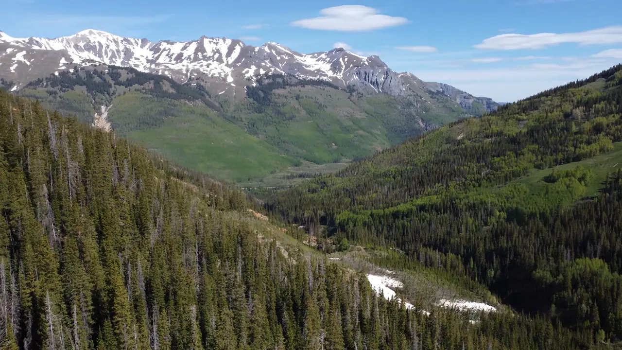 Aerial of snow-capped San Juan peaks above a green pine valley in Colorado