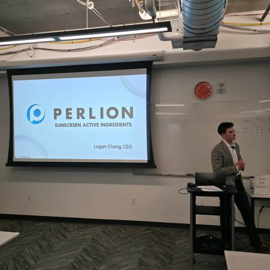 A projected title slide reading 'Perlion — Sunscreen Active Ingredients — Logan Chang, CEO,' with Chang standing beside a whiteboard to the right of the screen.