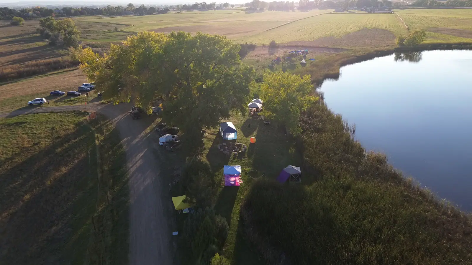 Golden-hour aerial of the 2023 Vybe outdoor festival beside a pond, colorful canopies below